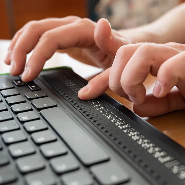 Mann schreibt auf einer Tastatur mit Braille-Zeile