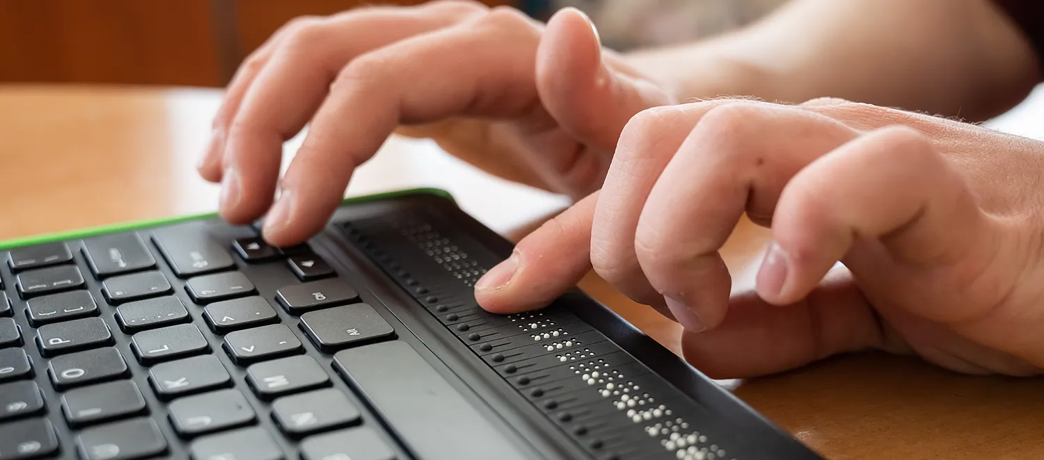 Mann schreibt auf einer Tastatur mit Braille-Zeile